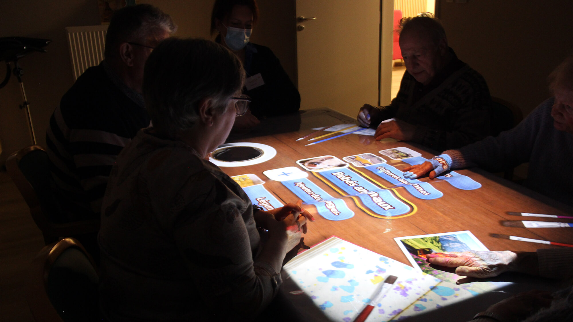 Un groupe de bénéficiaires autour de la Tovertafel, partageant un moment de convivialité et d’interaction sociale